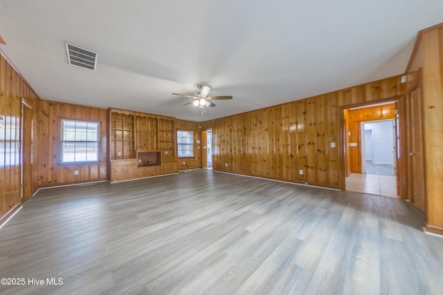 unfurnished living room with ceiling fan, wooden walls, a fireplace, and light wood-type flooring