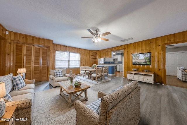 living room featuring ceiling fan, dark hardwood / wood-style floors, and wooden walls