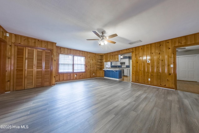 unfurnished living room with wood-type flooring, ceiling fan, and wood walls