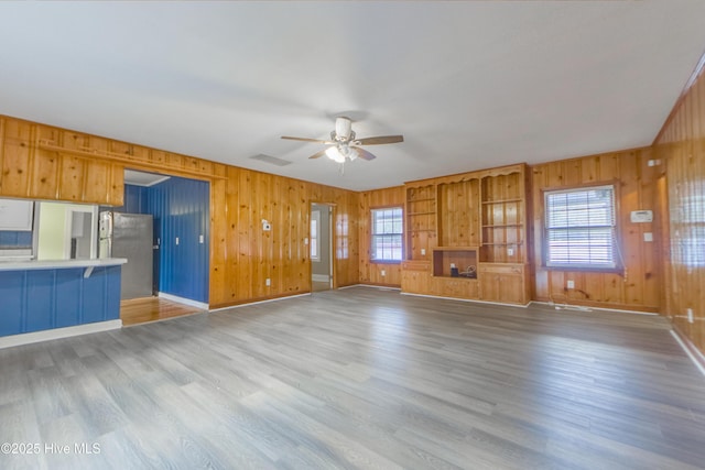 unfurnished living room with hardwood / wood-style flooring, ceiling fan, wooden walls, and a wealth of natural light