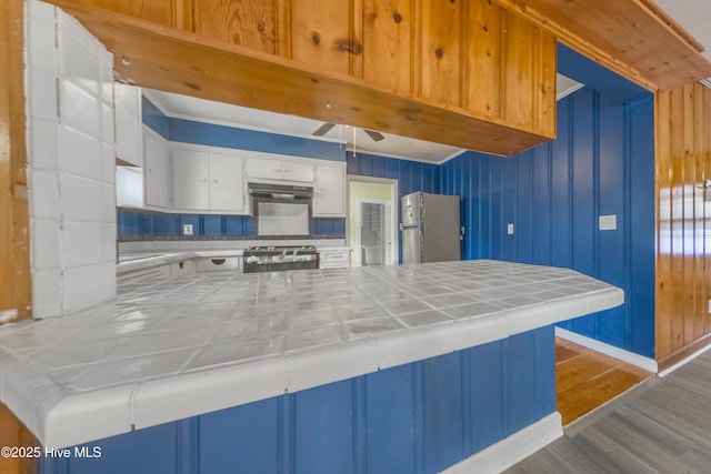 kitchen with appliances with stainless steel finishes, tile countertops, white cabinets, ceiling fan, and light hardwood / wood-style floors