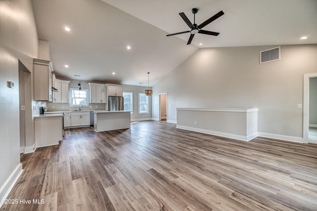 unfurnished living room with ceiling fan, high vaulted ceiling, sink, and light hardwood / wood-style flooring