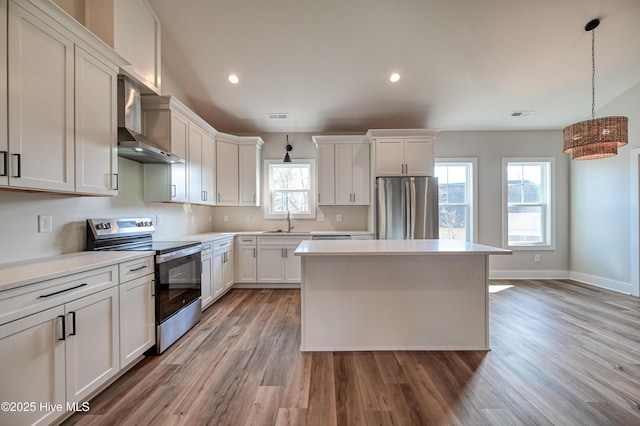 kitchen with white cabinetry, hanging light fixtures, stainless steel appliances, and wall chimney exhaust hood