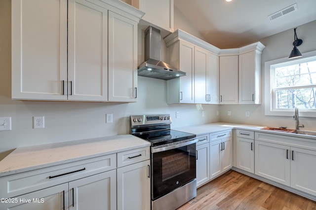kitchen with wall chimney range hood, a sink, stainless steel electric stove, white cabinetry, and visible vents