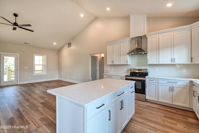 kitchen featuring stainless steel electric range oven, a kitchen island, white cabinets, light stone countertops, and wall chimney range hood