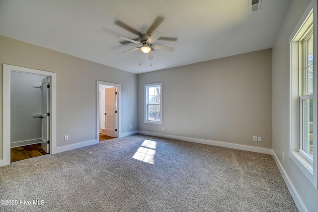 unfurnished bedroom with a walk in closet, ceiling fan, baseboards, dark colored carpet, and visible vents