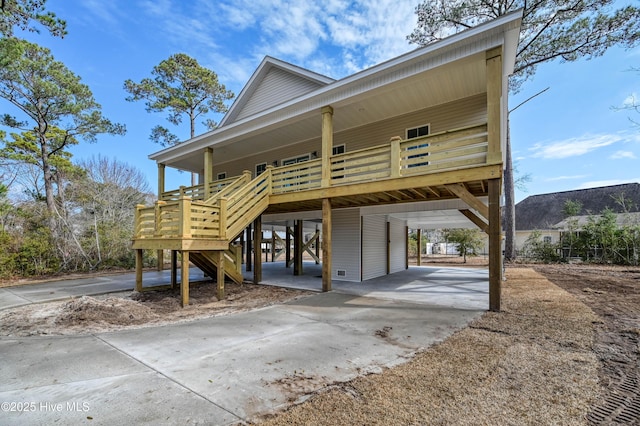 coastal inspired home featuring a carport, covered porch, stairs, and concrete driveway