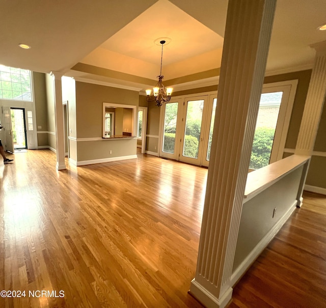 interior space with a tray ceiling, a wealth of natural light, wood-type flooring, and ornate columns