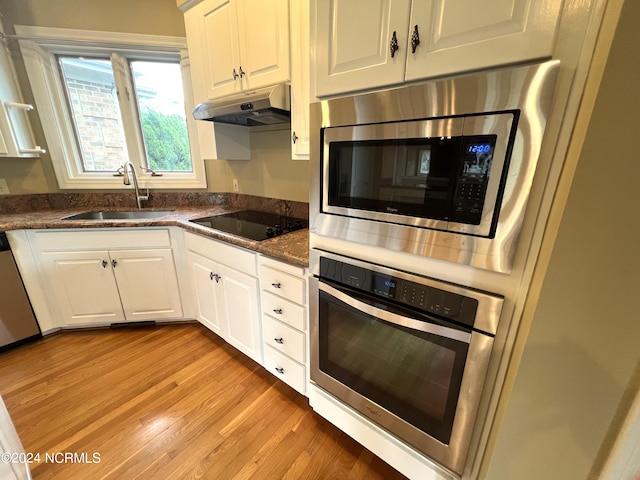 kitchen with sink, white cabinetry, light wood-type flooring, appliances with stainless steel finishes, and dark stone counters