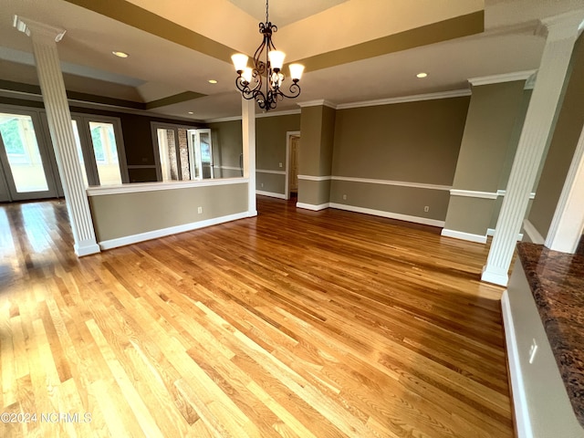 interior space featuring a raised ceiling, crown molding, wood-type flooring, and decorative columns