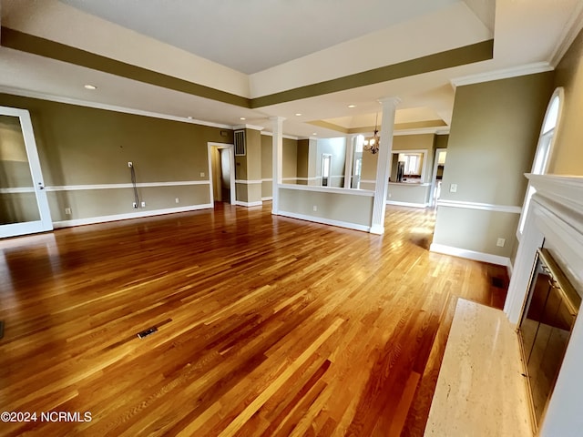 unfurnished living room with ornate columns, hardwood / wood-style floors, ornamental molding, a raised ceiling, and an inviting chandelier