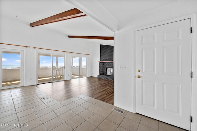 tiled spare room featuring beamed ceiling and a brick fireplace