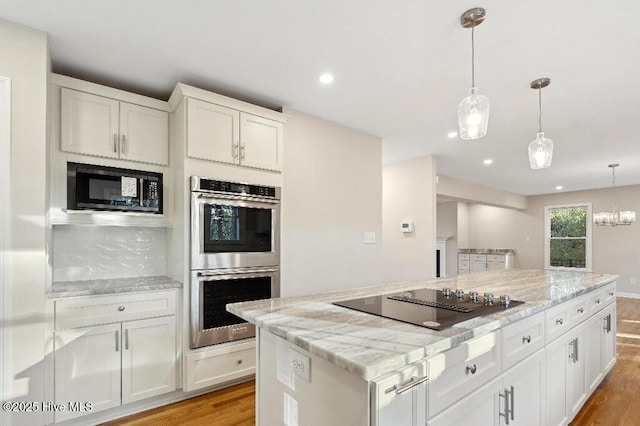 kitchen with light stone counters, black appliances, white cabinets, a kitchen island, and decorative light fixtures