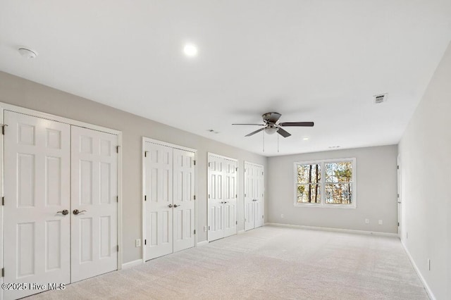 unfurnished bedroom featuring ceiling fan, light colored carpet, and two closets