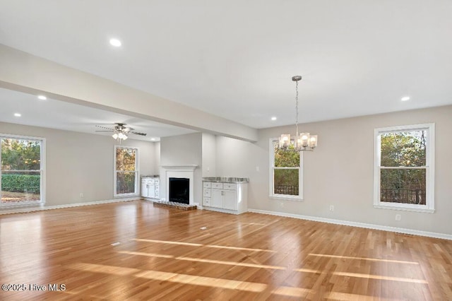 unfurnished living room featuring ceiling fan with notable chandelier and light wood-type flooring