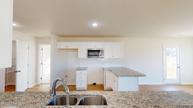 kitchen featuring tasteful backsplash, sink, white cabinets, light stone counters, and light hardwood / wood-style flooring