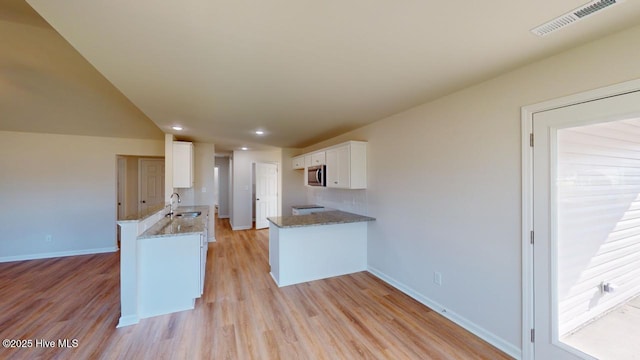 kitchen with sink, white cabinets, light stone counters, and kitchen peninsula