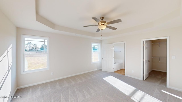 unfurnished bedroom with ensuite bath, a tray ceiling, light carpet, a walk in closet, and a closet