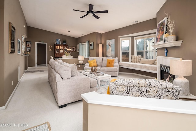 carpeted living room with a tiled fireplace, vaulted ceiling, and ceiling fan