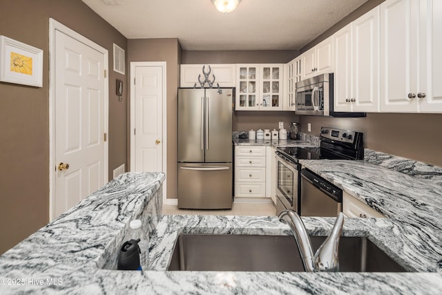 kitchen featuring appliances with stainless steel finishes, sink, white cabinets, light tile patterned floors, and light stone countertops