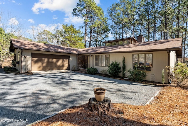 mid-century home with driveway, a chimney, and an attached garage