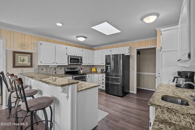 kitchen with stainless steel appliances, white cabinets, a sink, light stone countertops, and a peninsula