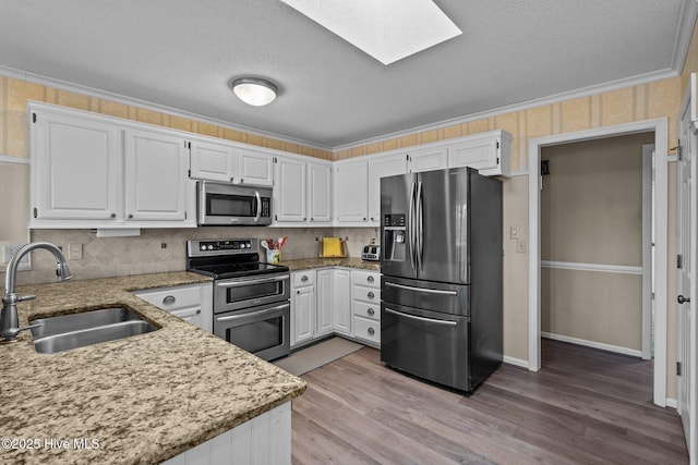 kitchen featuring stainless steel appliances, a skylight, white cabinetry, and a sink