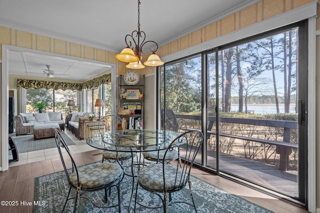 dining room featuring ceiling fan with notable chandelier, ornamental molding, a water view, and wood finished floors