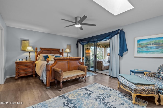 bedroom featuring a skylight, ceiling fan, wood finished floors, access to outside, and baseboards