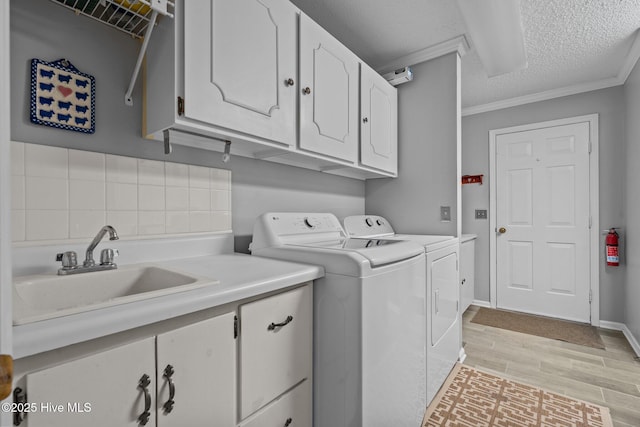 laundry room with a textured ceiling, a sink, light wood-style floors, cabinet space, and washer and clothes dryer