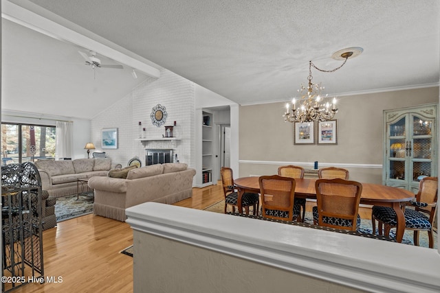 dining room featuring a textured ceiling, light wood-type flooring, a brick fireplace, and vaulted ceiling with beams