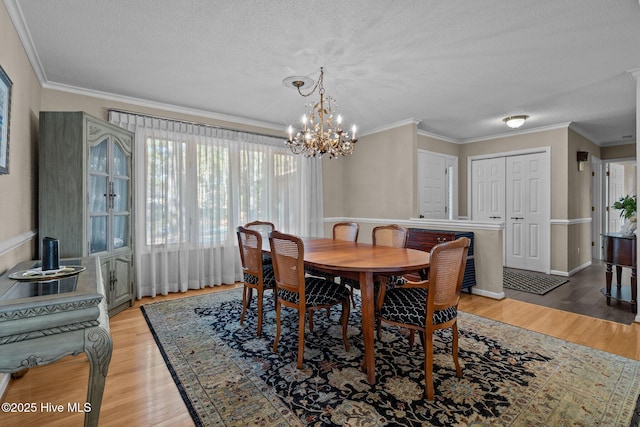 dining area with light wood-type flooring, an inviting chandelier, ornamental molding, and a textured ceiling