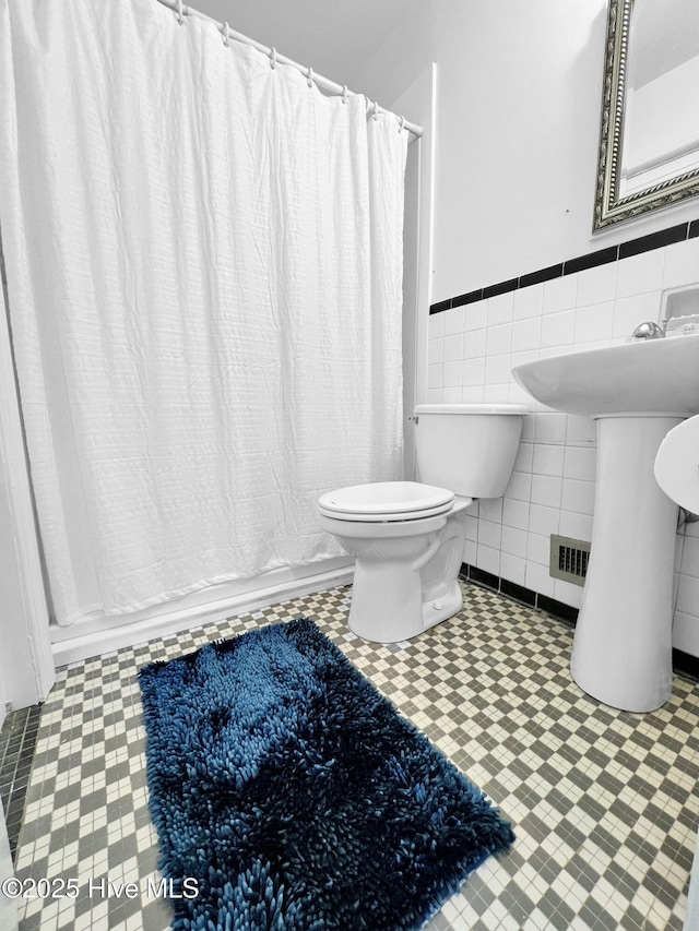 full bath featuring a shower with curtain, a wainscoted wall, tile walls, and toilet