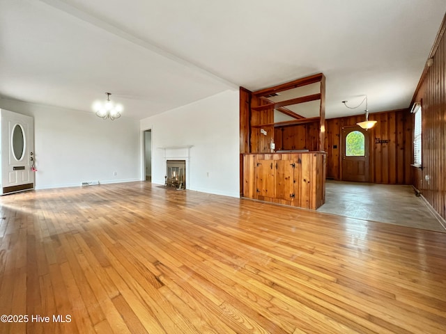 unfurnished living room featuring a notable chandelier, visible vents, wood walls, light wood-type flooring, and a warm lit fireplace