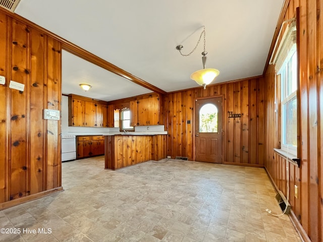 kitchen featuring a peninsula, wood walls, brown cabinetry, and a wealth of natural light