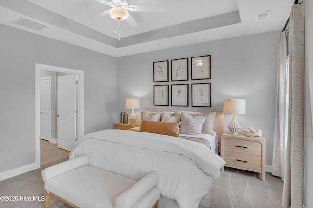 bedroom with light colored carpet, a tray ceiling, visible vents, and baseboards