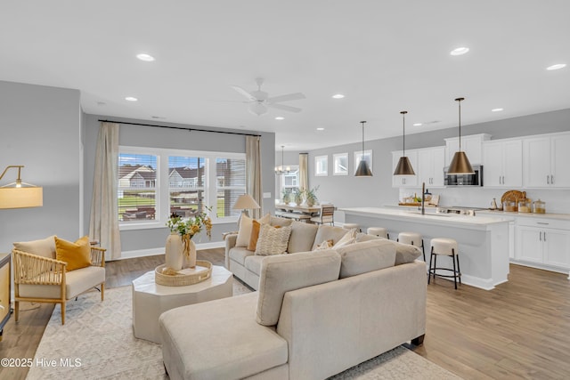 living room featuring light wood-style floors, ceiling fan with notable chandelier, baseboards, and recessed lighting