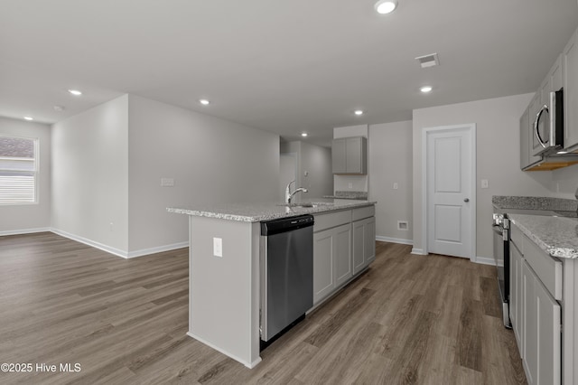 6986 Seaside Palms Pl SW, Sunset Beach, NC 28468 - kitchen with appliances with stainless steel finishes, light wood-type flooring, a kitchen island with sink, recessed lighting, and light stone counters