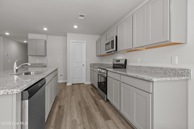 6986 Seaside Palms Pl SW, Sunset Beach, NC 28468 - kitchen with stainless steel appliances, light wood finished floors, light stone counters, recessed lighting, and a center island with sink