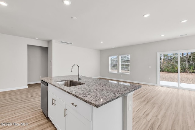 kitchen featuring white cabinetry, sink, a kitchen island with sink, stainless steel dishwasher, and light stone countertops