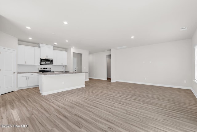 kitchen featuring white cabinetry, light stone counters, a kitchen island with sink, stainless steel appliances, and light hardwood / wood-style floors