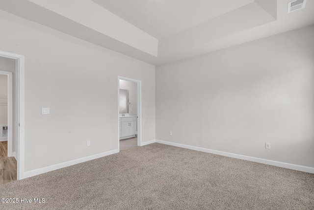 unfurnished bedroom with light colored carpet, a tray ceiling, and ensuite bath