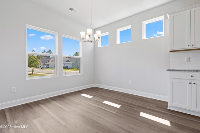 unfurnished dining area with dark wood-type flooring, visible vents, baseboards, and an inviting chandelier