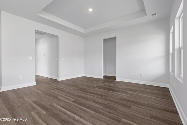 empty room with dark wood-style floors, baseboards, visible vents, and a raised ceiling