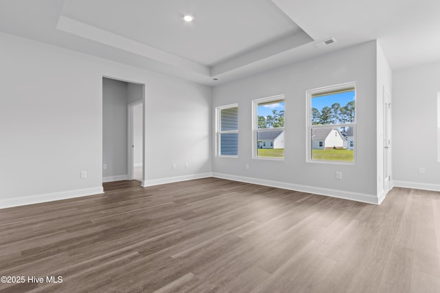 empty room featuring a tray ceiling, wood finished floors, visible vents, and baseboards