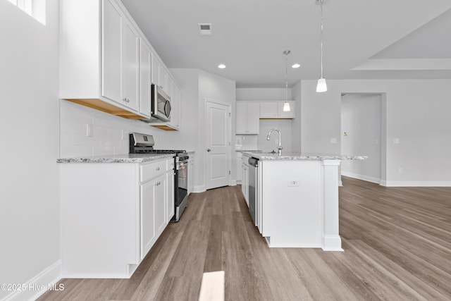 kitchen with stainless steel appliances, visible vents, backsplash, light stone countertops, and light wood-type flooring