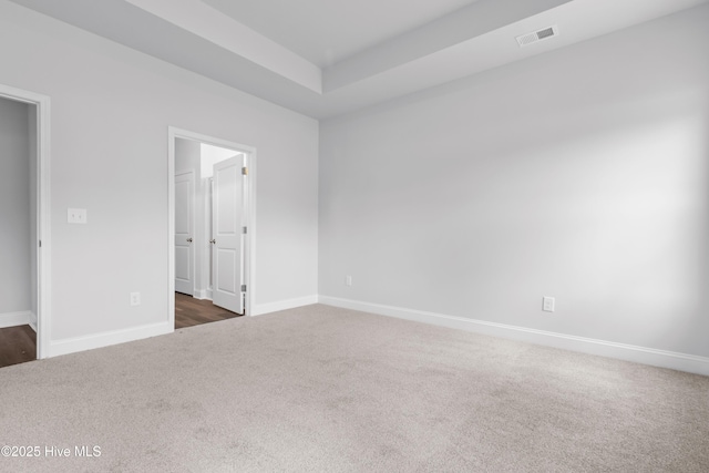 empty room featuring dark colored carpet, a tray ceiling, visible vents, and baseboards