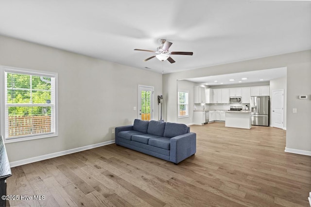 living area with light wood-type flooring, a ceiling fan, baseboards, and recessed lighting