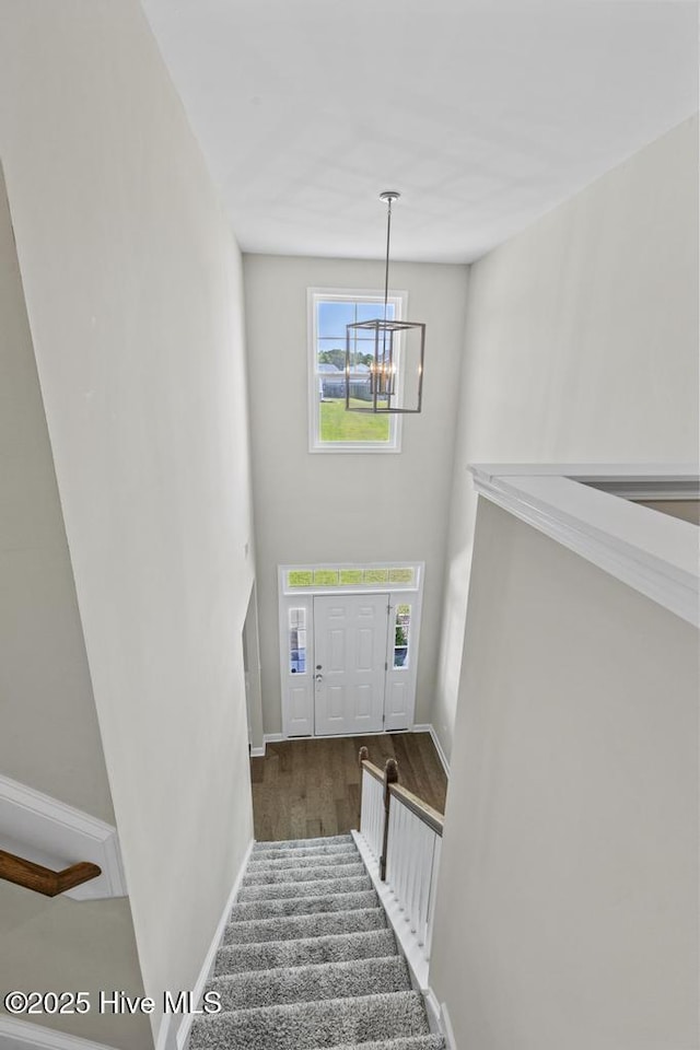 stairway featuring baseboards, a towering ceiling, wood finished floors, and a chandelier
