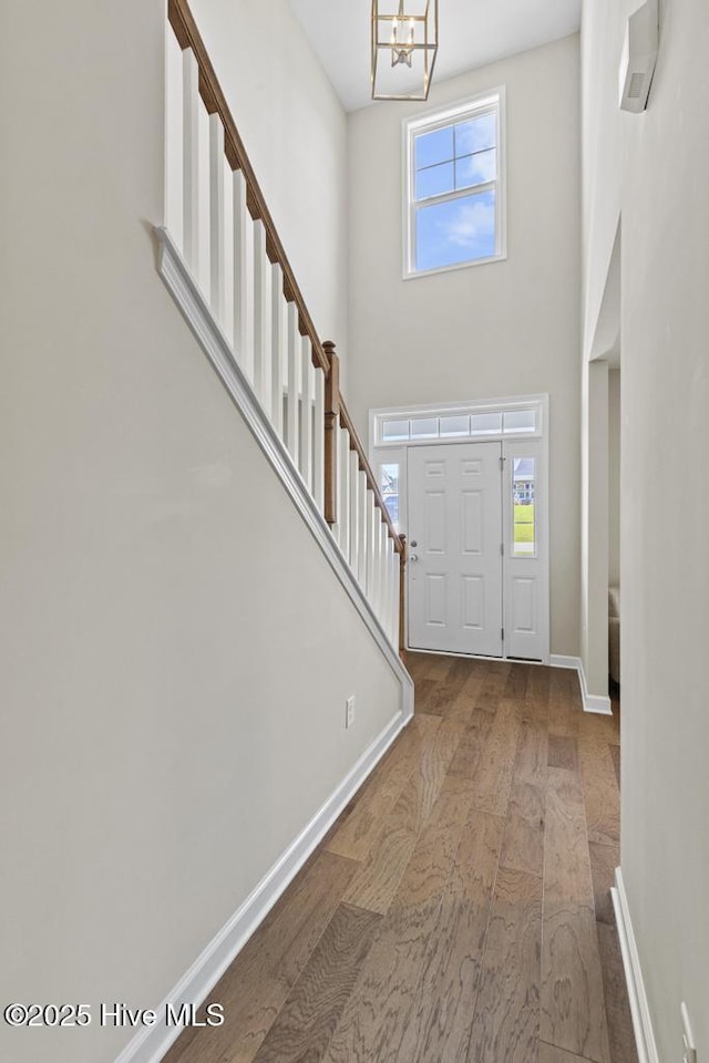 entryway with an inviting chandelier, baseboards, wood finished floors, and a towering ceiling